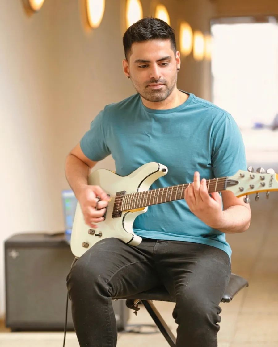 Rohith playing an electric guitar, seated in a rehearsal room